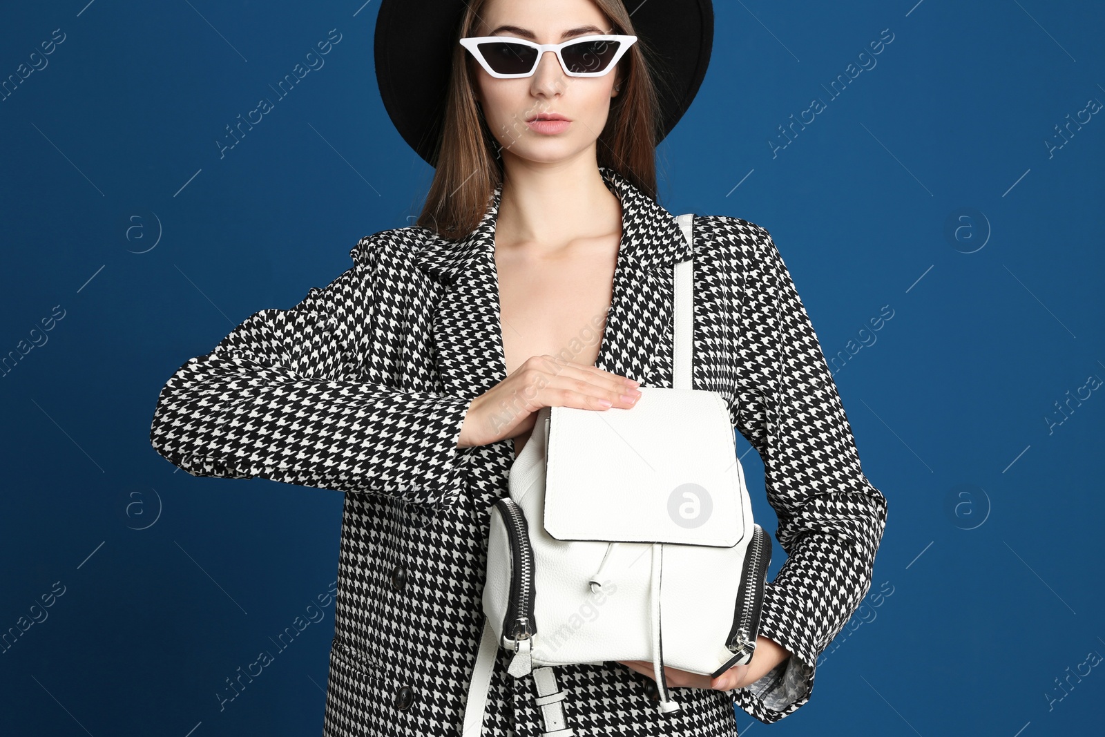 Photo of Beautiful young woman in sunglasses with stylish bag on blue background