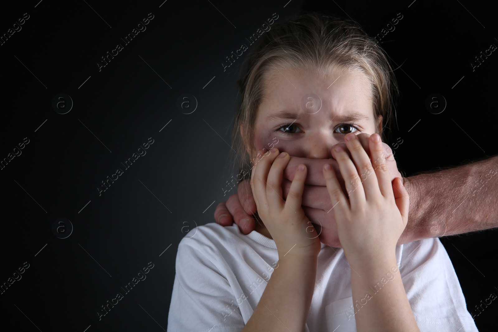 Photo of Man covering scared little girl's mouth on black background, space for text. Domestic violence