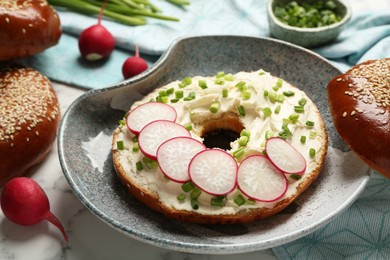 Photo of Delicious bagel with cream cheese, green onion and radish on plate, closeup