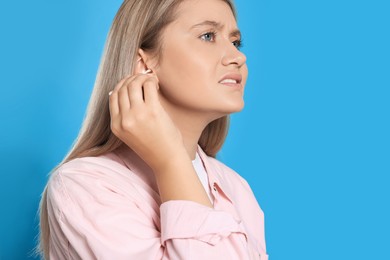 Young woman cleaning ear with cotton swab on light blue background. Space for text