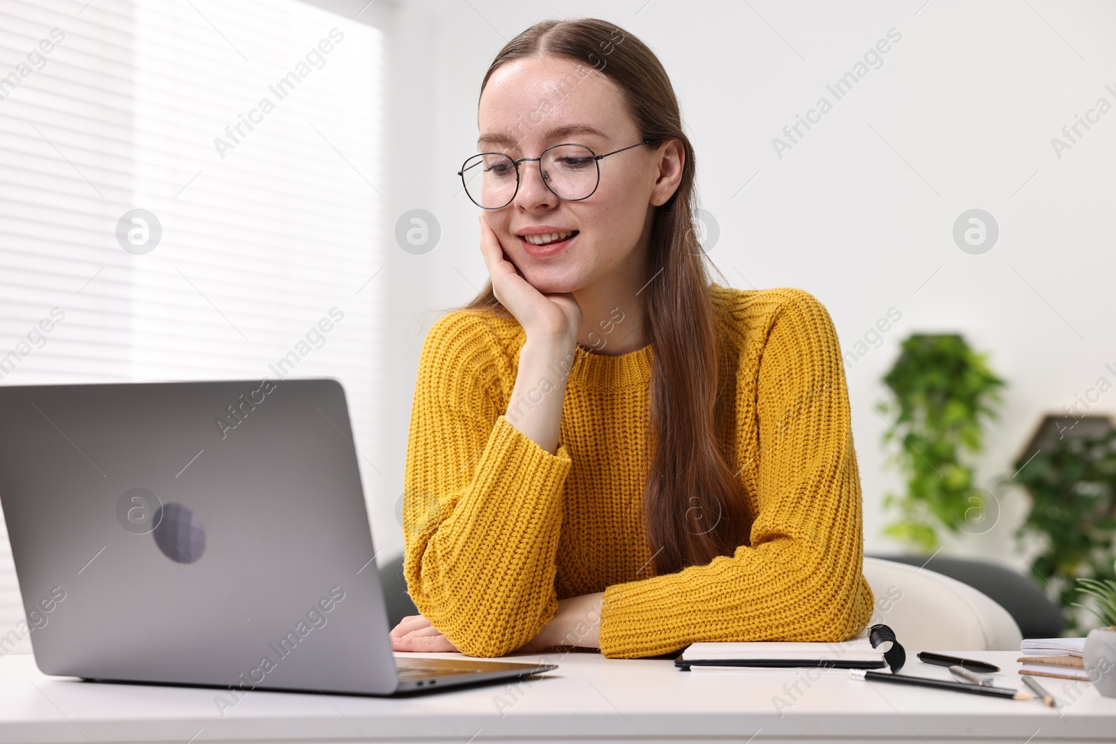 Photo of E-learning. Young woman using laptop during online lesson at white table indoors