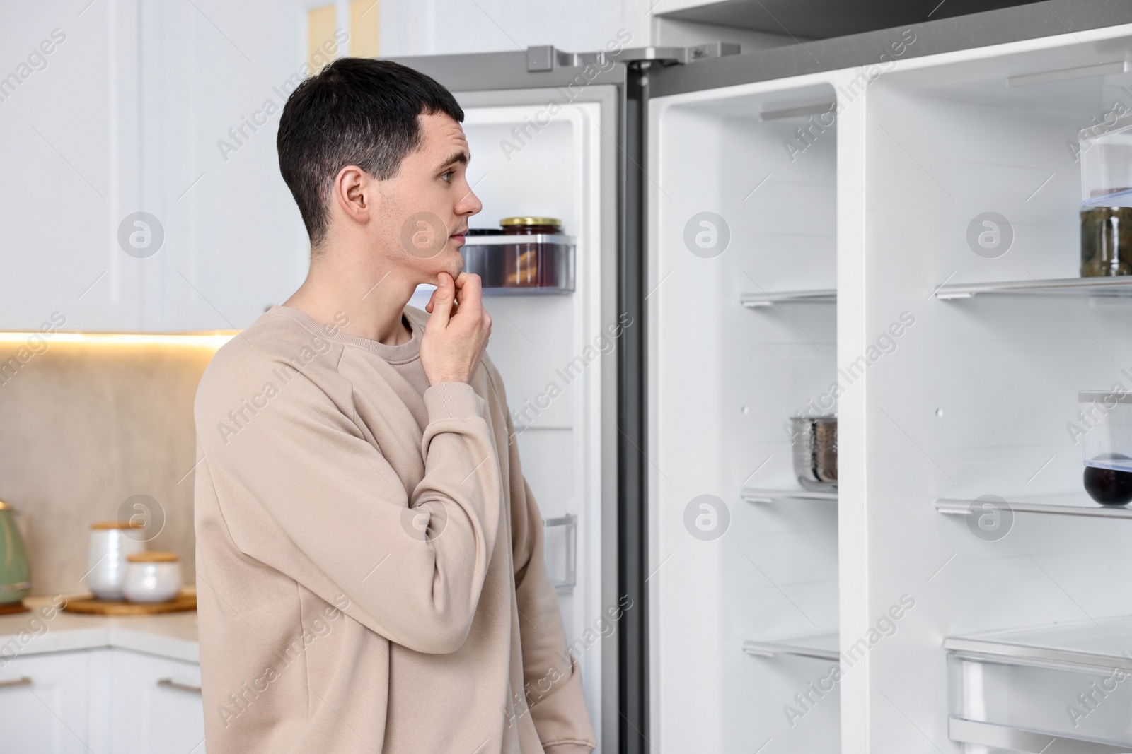 Photo of Thoughtful man near empty refrigerator in kitchen