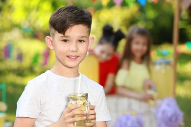 Cute little boy with natural lemonade in park, space for text. Summer refreshing drink