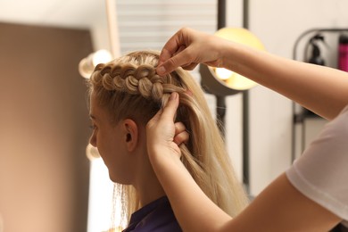 Professional stylist braiding client's hair in salon