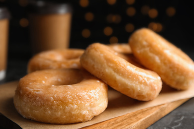 Photo of Delicious glazed donuts on wooden board, closeup