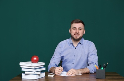 Portrait of young teacher at table against green background. Space for text