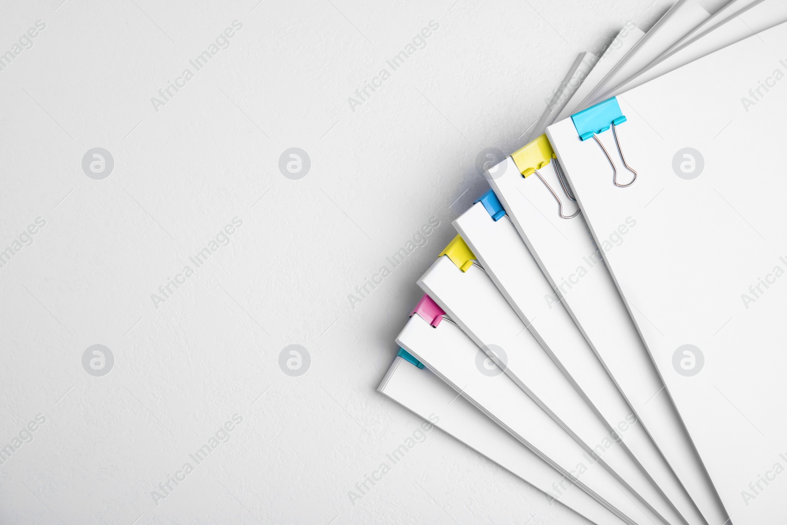 Photo of Many sheets of paper with colorful clips on white background, top view. Space for text