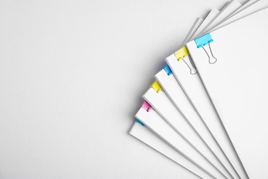 Photo of Many sheets of paper with colorful clips on white background, top view. Space for text