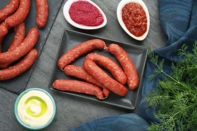 Photo of Tasty sausages, different sauces and dill on black table, flat lay. Meat product