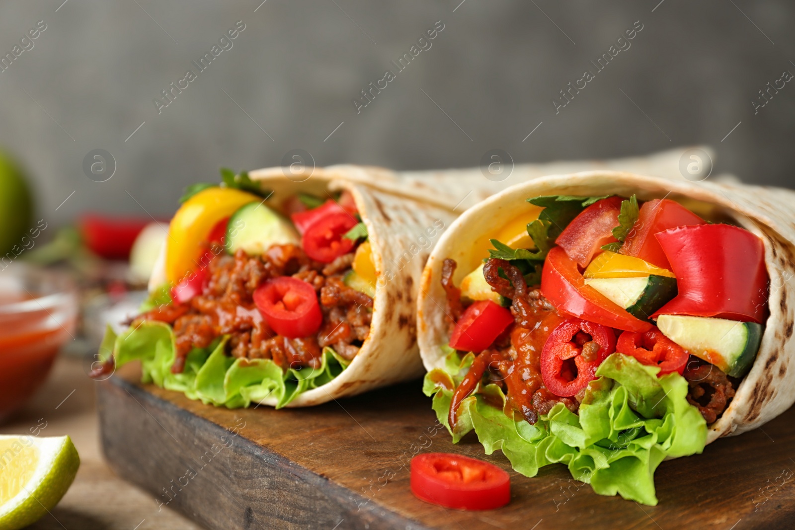 Photo of Board with delicious meat tortilla wraps on table, closeup