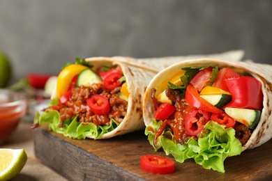 Board with delicious meat tortilla wraps on table, closeup