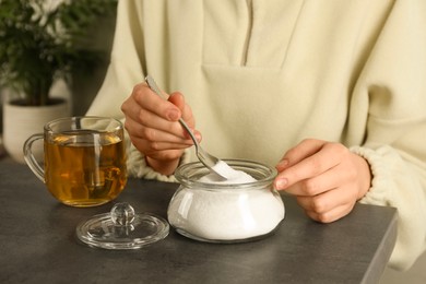 Woman adding sugar into aromatic tea at grey table indoors, closeup