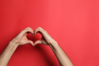 Photo of Man making heart with his hands on red background, closeup. Space for text