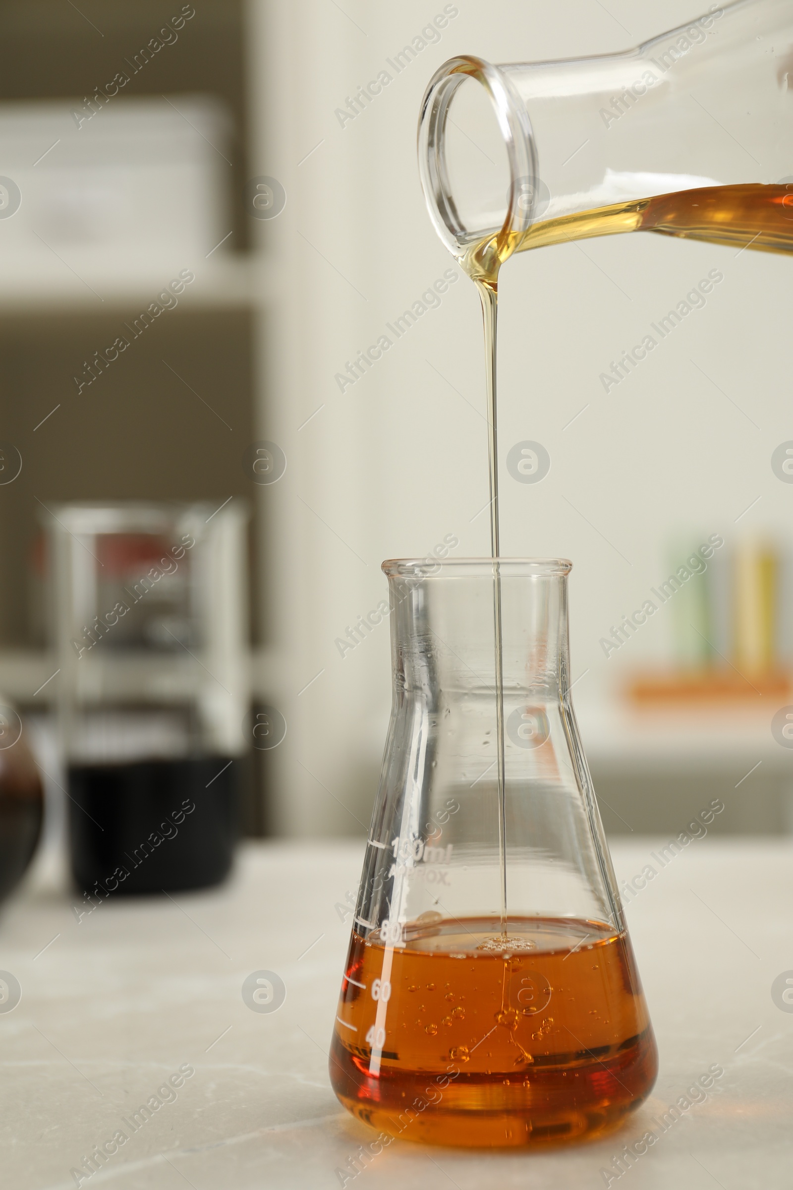 Photo of Pouring orange crude oil into flask at light marble table, closeup