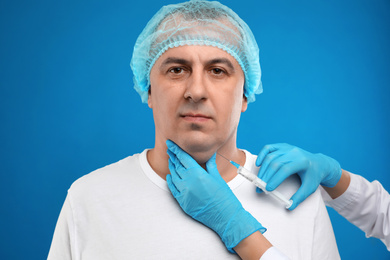 Mature man with double chin receiving injection on blue background