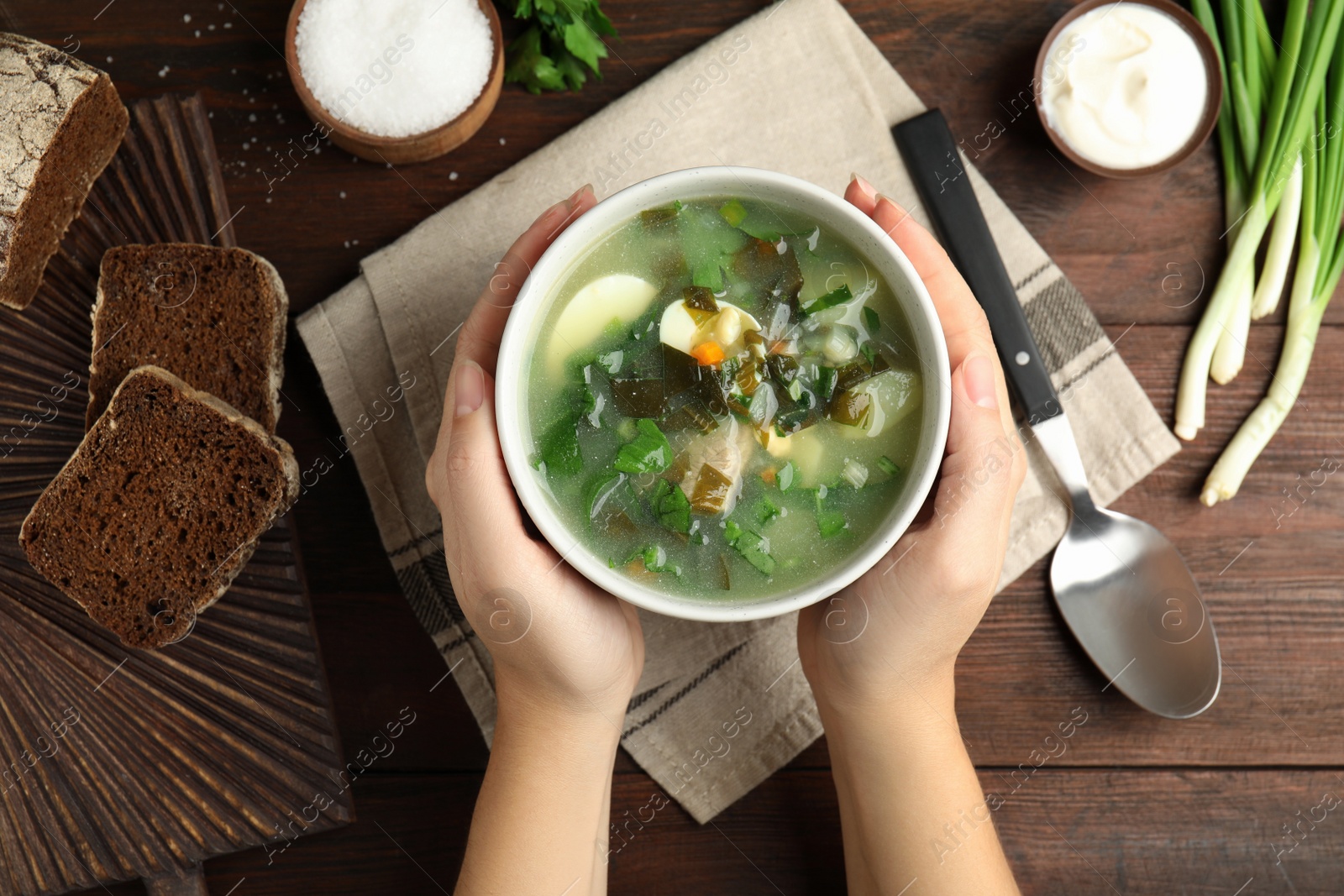 Photo of Woman eating delicious sorrel soup at brown wooden table, top view