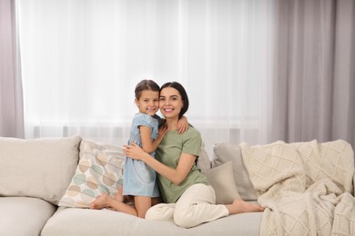 Photo of Happy woman and her cute daughter spending time together on sofa at home. Mother's day celebration