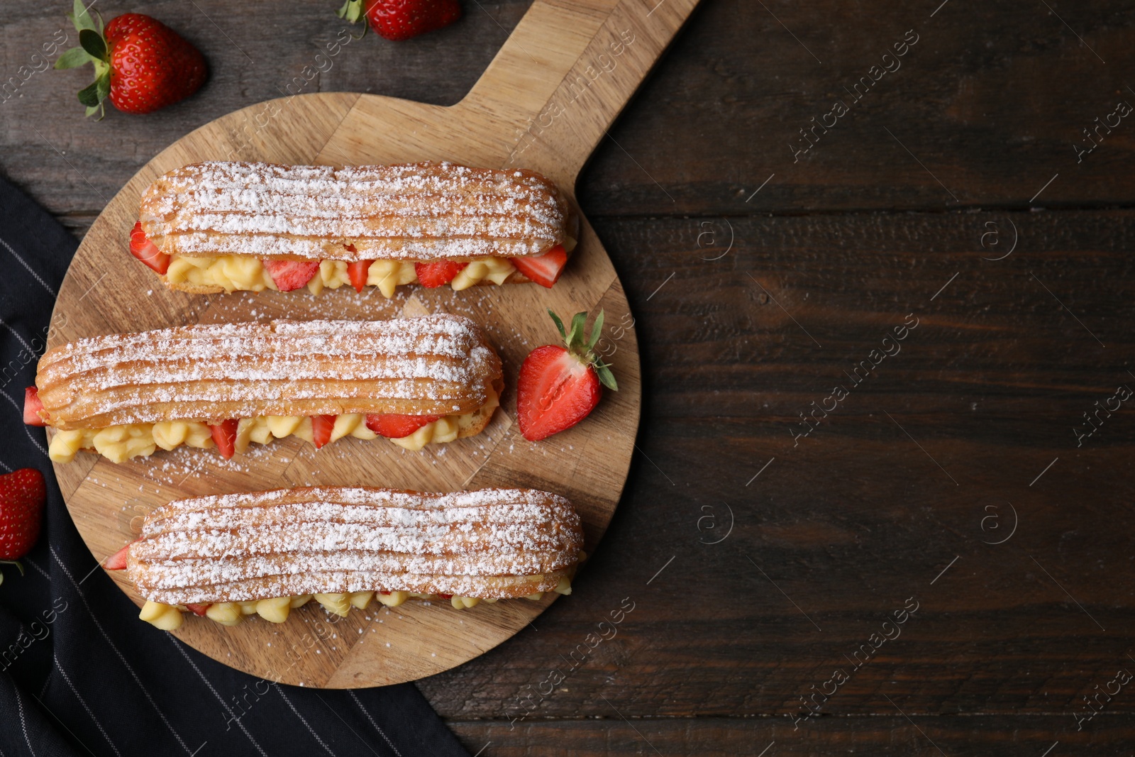 Photo of Delicious eclairs filled with cream and strawberries on wooden table, top view. Space for text