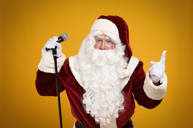 Photo of Santa Claus singing with microphone on yellow background. Christmas music