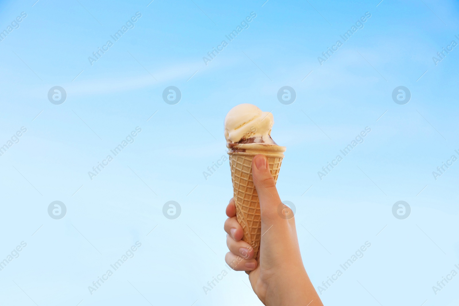 Photo of Woman holding waffle cone with delicious ice cream against blue sky on city street, closeup