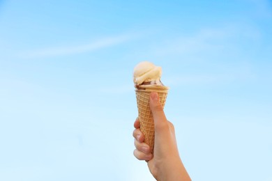 Woman holding waffle cone with delicious ice cream against blue sky on city street, closeup