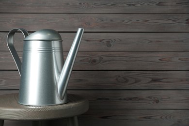 Metal watering can on table against grey wooden background, space for text