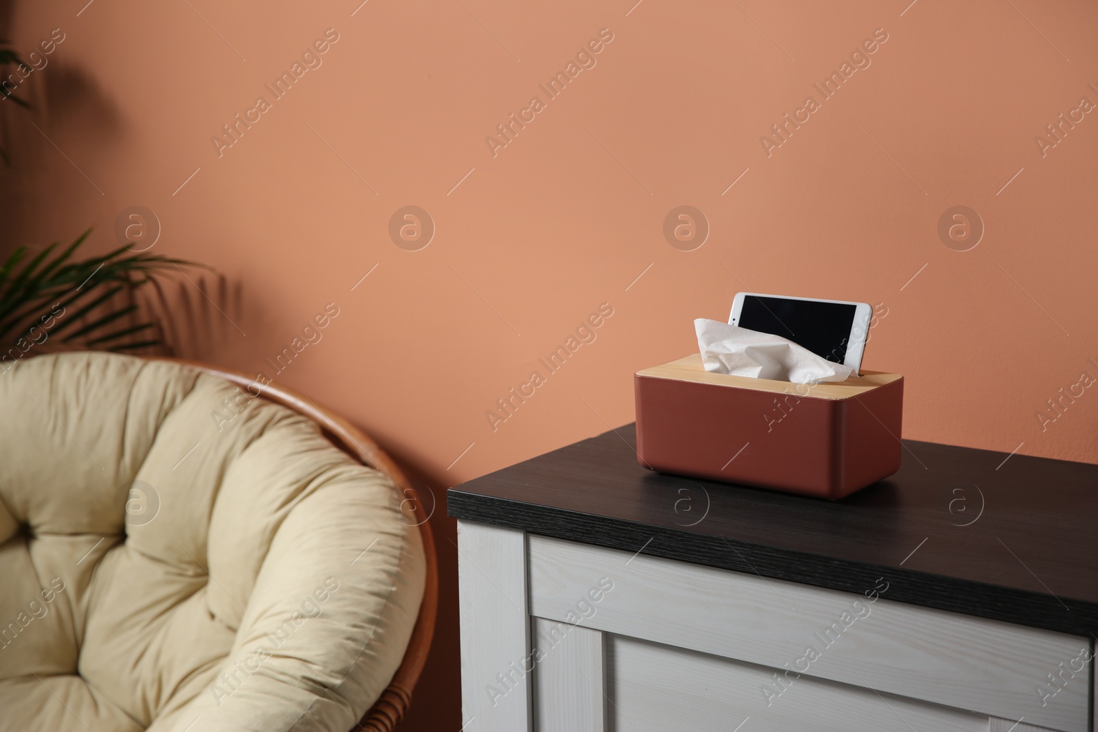 Photo of Box with paper tissues and smartphone on wooden cabinet in room