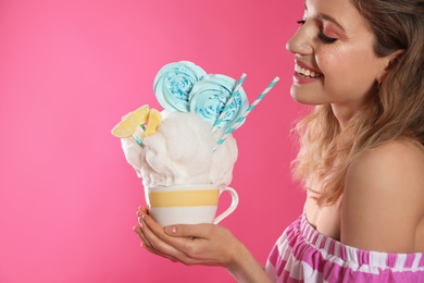 Young woman with tasty cotton candy on pink background, closeup. Space for text