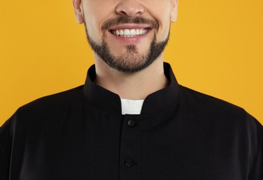 Photo of Priest wearing cassock with clerical collar on yellow background, closeup