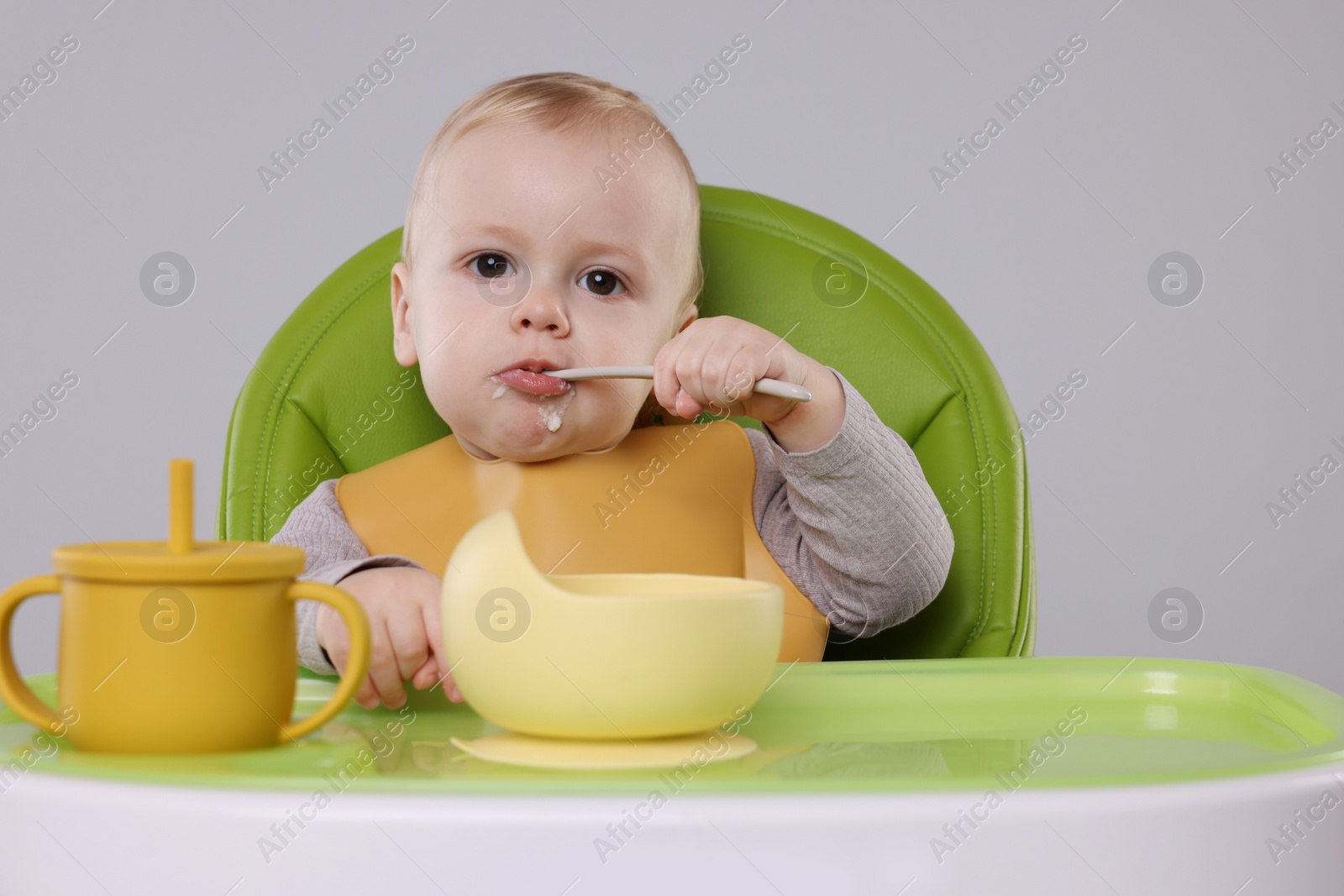 Photo of Cute little baby eating healthy food in high chair on gray background