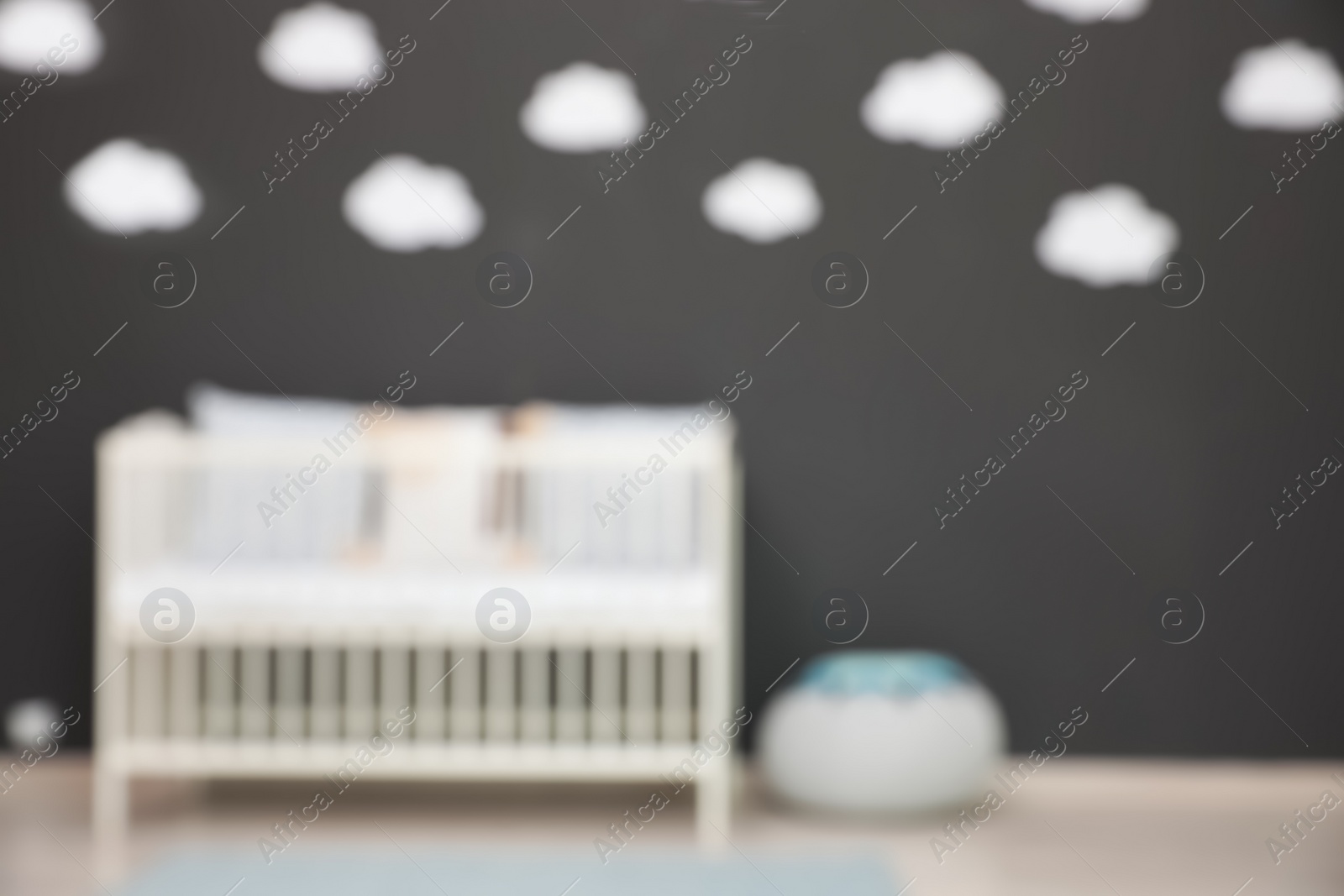 Photo of Blurred view of cute baby room interior with modern crib near dark wall