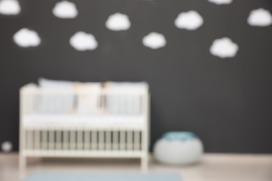 Blurred view of cute baby room interior with modern crib near dark wall