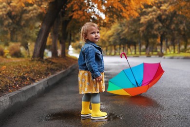Photo of Cute little girl standing in puddle near colorful umbrella outdoors