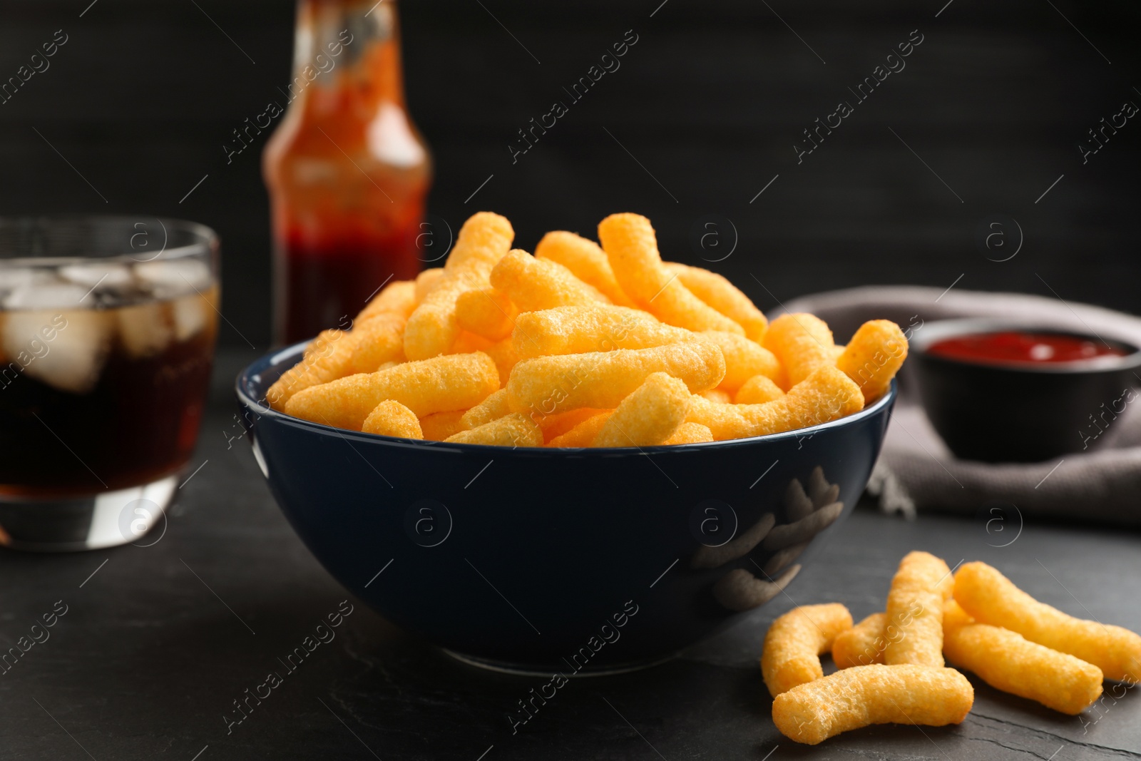 Photo of Bowl with crunchy cheesy corn snack on black table, closeup