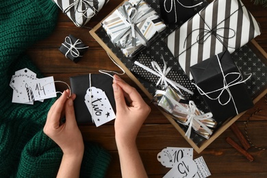 Woman decorating gift box at wooden table, top view. Creating advent calendar