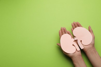 Photo of Woman holding paper cutout of kidneys on green background, top view. Space for text