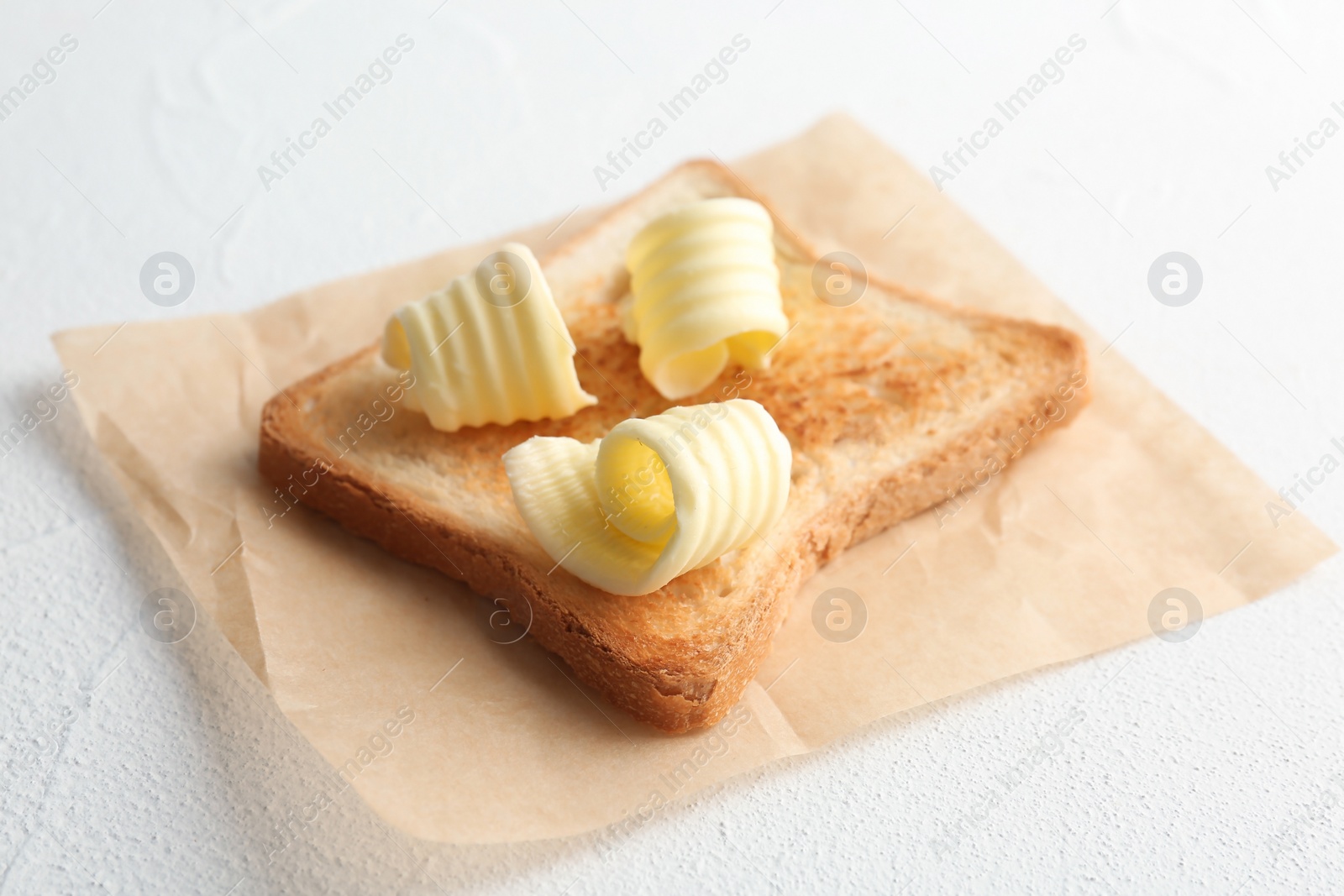 Photo of Toasted bread with fresh butter curls on table, closeup