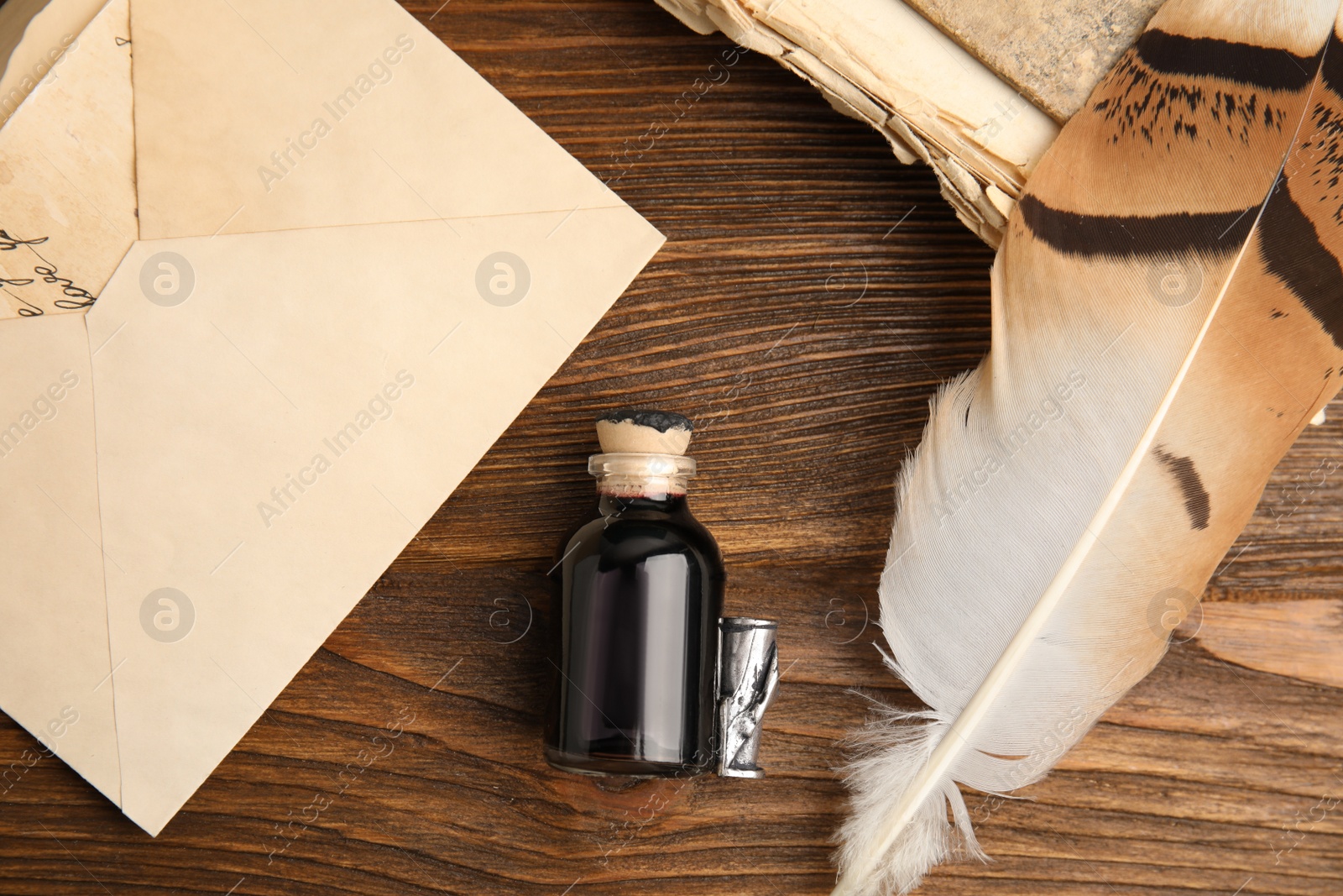 Photo of Feather pen, bottle of ink and old paper on wooden table, flat lay