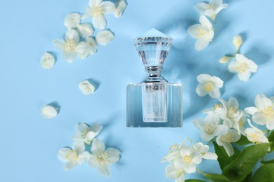 Aromatic perfume in bottle and beautiful jasmine flowers on light blue background, flat lay