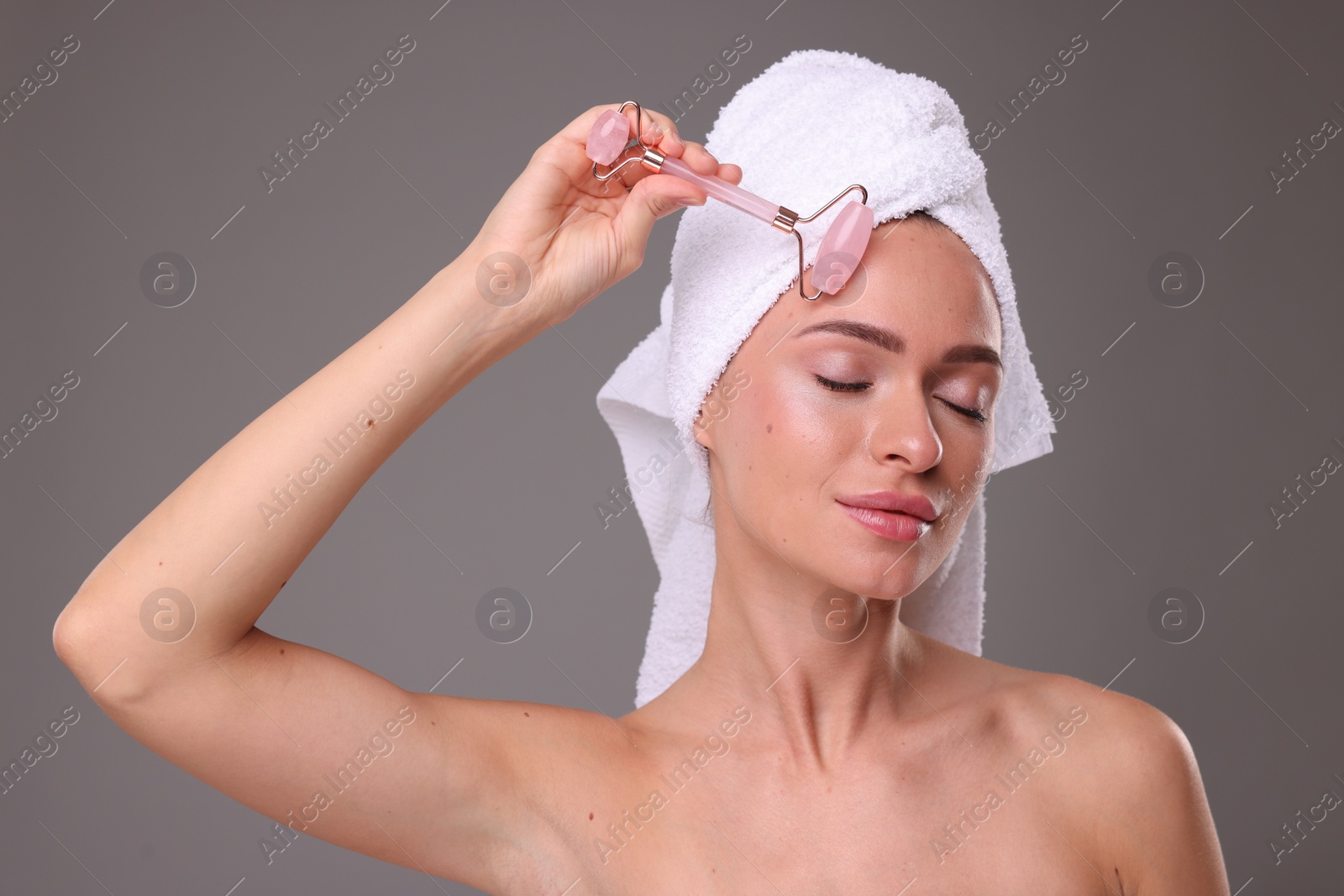 Photo of Young woman massaging her face with rose quartz roller on grey background