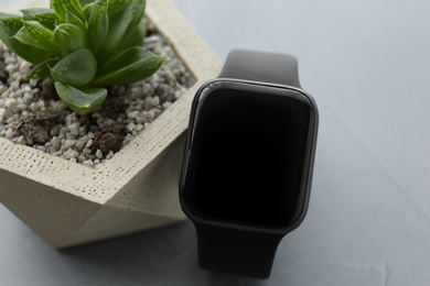 Photo of Stylish smart watch and plant on grey table, closeup