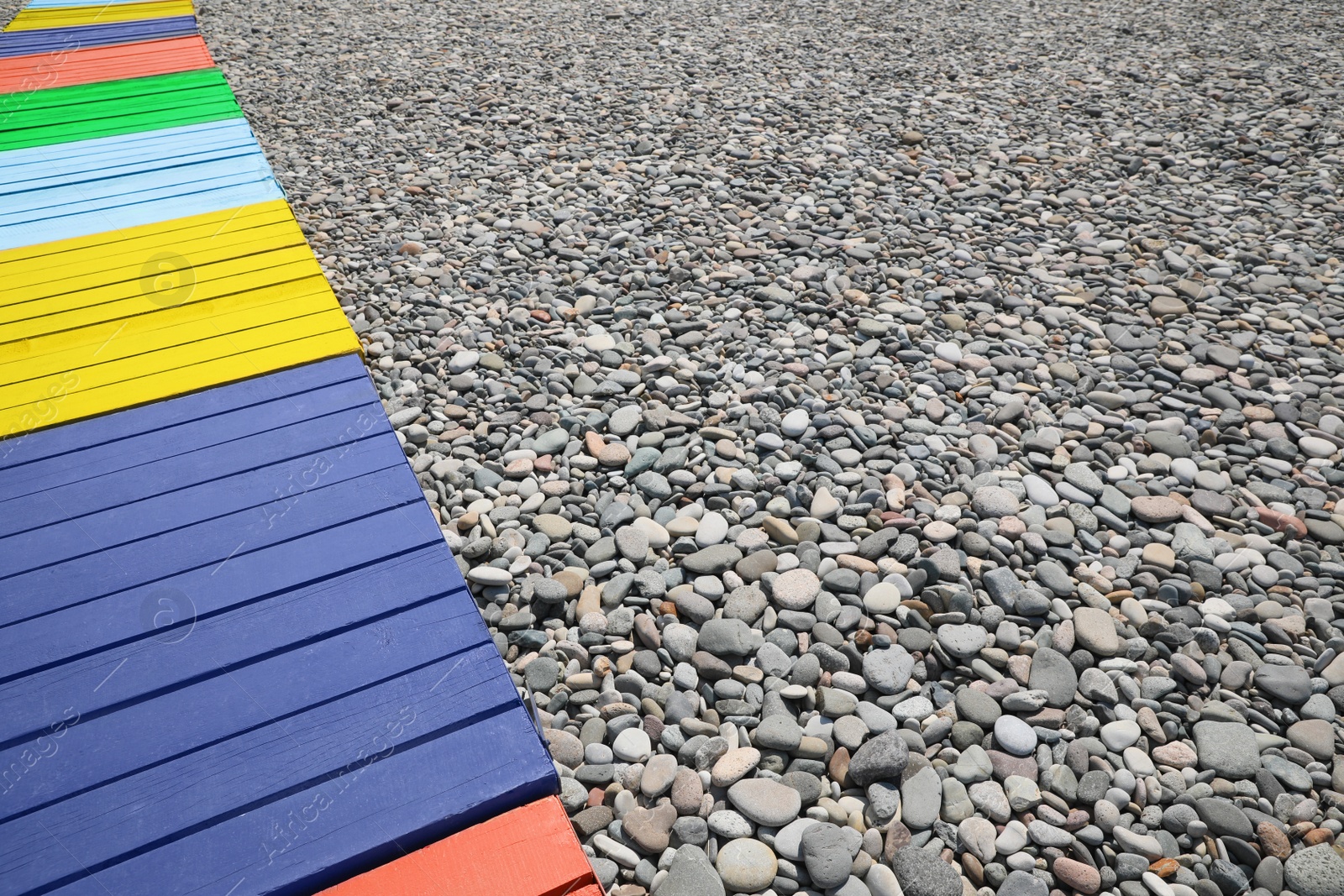 Photo of Colorful wooden walkway on pebble beach. Space for text