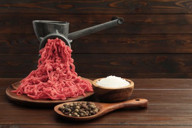 Photo of Meat grinder with beef mince and spices on wooden table, space for text