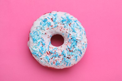 Sweet glazed donut decorated with sprinkles on pink background, top view. Tasty confectionery