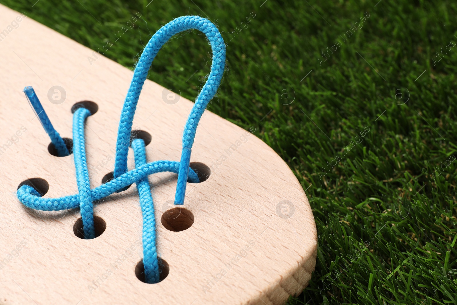 Photo of Wooden lacing toy on artificial grass, closeup. Educational toy for motor skills development