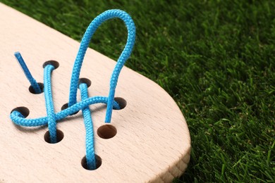 Photo of Wooden lacing toy on artificial grass, closeup. Educational toy for motor skills development