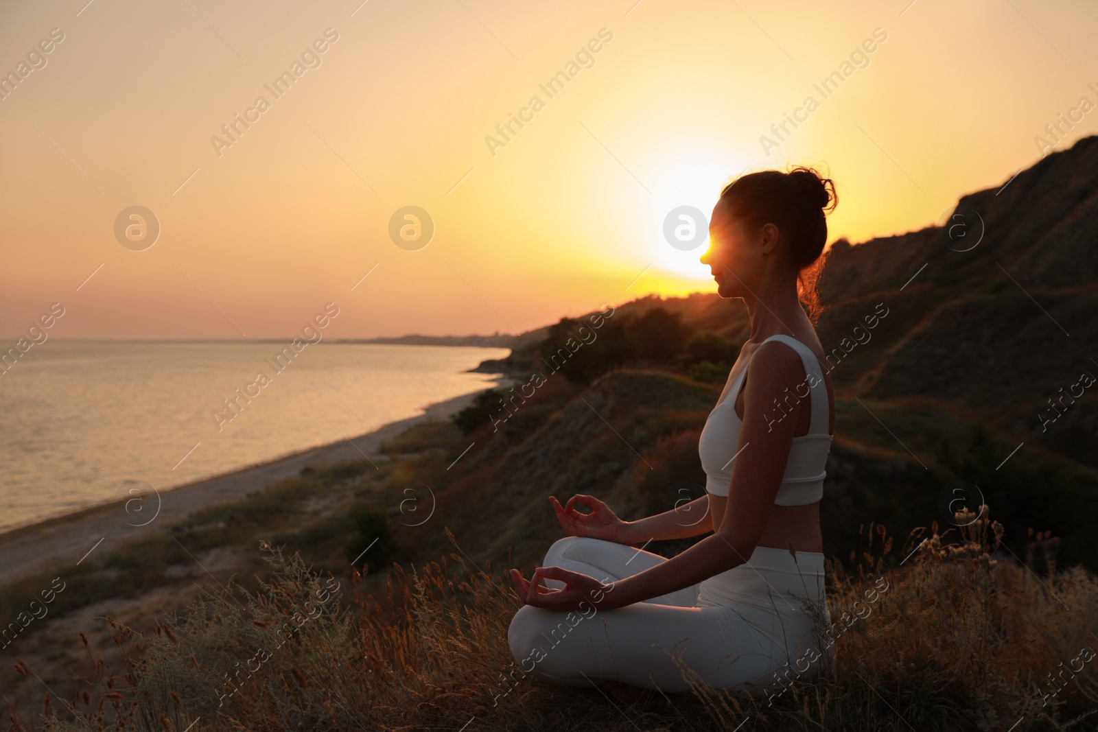 Photo of Mature woman meditating on hill near sea at sunset. Space for text