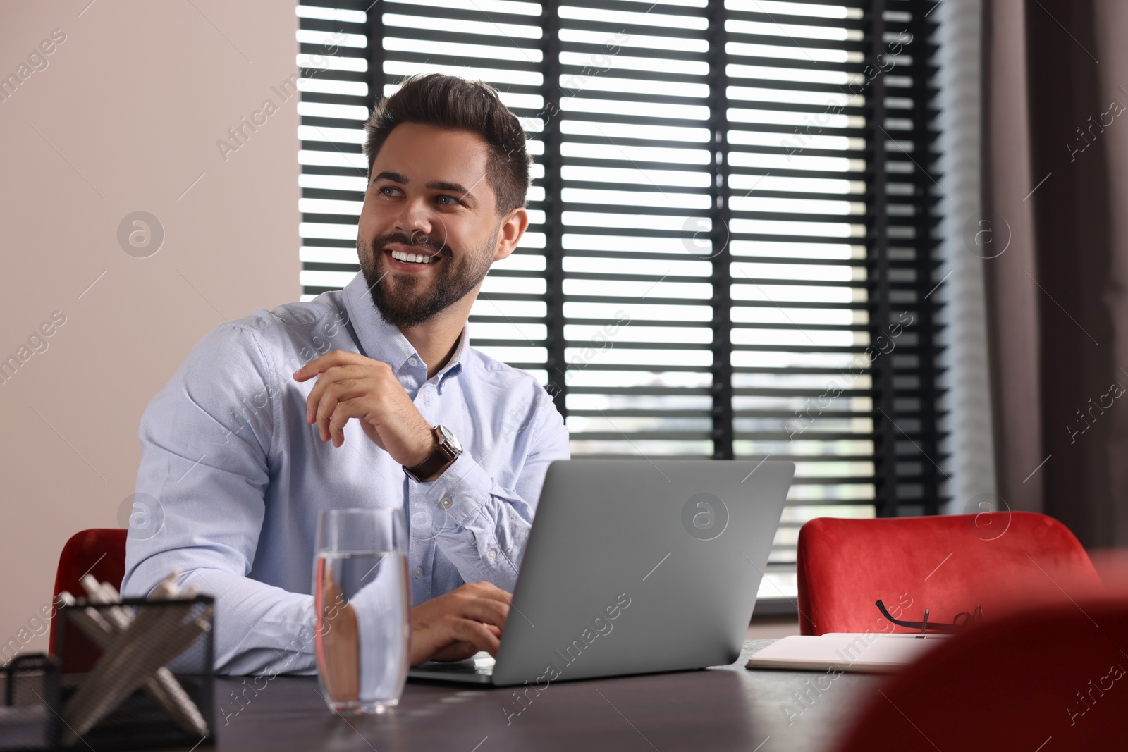 Photo of Happy young man working on laptop at table in office