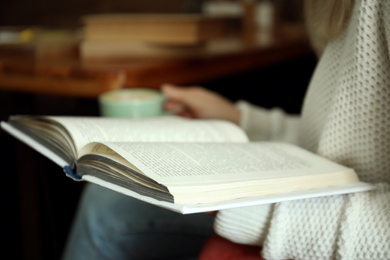 Photo of Woman with cup of coffee reading book indoors, closeup