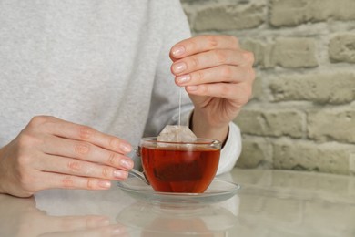 Woman taking tea bag out of cup at table indoors, closeup